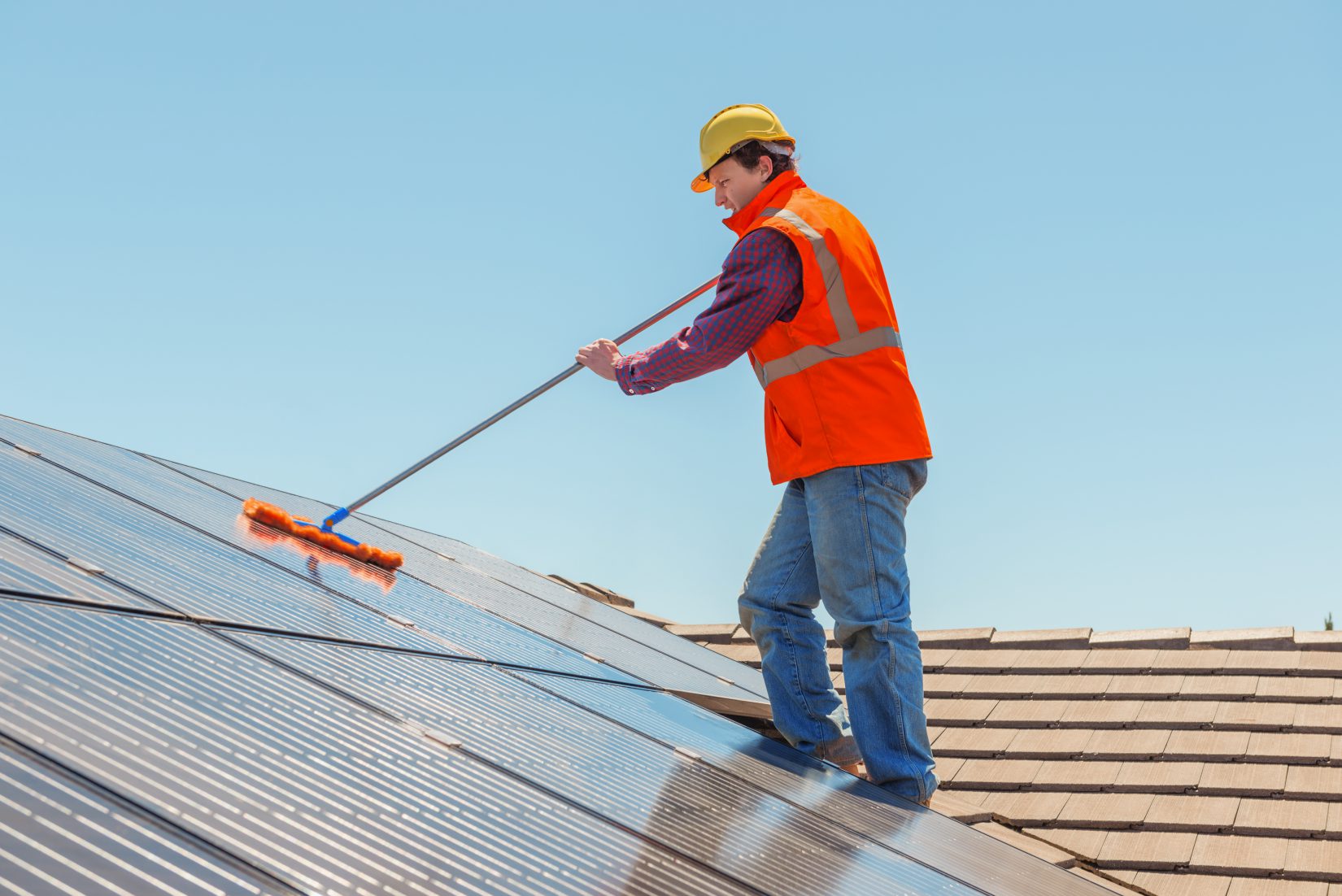 worker cleaning a solar panel on roof