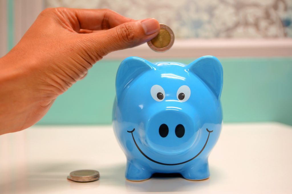 person dropping coins into a blue piggy bank